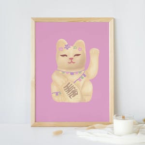 May include: A framed print featuring a cream-colored Maneki-neko cat with a raised paw, adorned with floral accents. The cat holds a banner with Japanese characters, set against a pink background. The artwork is in a wooden frame.