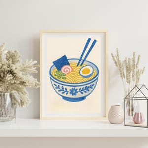 May include: A framed illustration of a bowl of ramen with chopsticks, a soft boiled egg, seaweed, and a pink fish cake. The bowl is blue and white with a floral design.