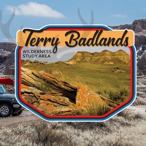 May include: A vinyl decal featuring the text "Terry Badlands Wilderness Study Area" with a scenic landscape illustration. The decal also includes the text "Stuck On Travel Vinyl Decals Travel Memories". A vehicle with a canoe is parked on a road.