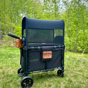 Peut inclure: Un chariot pliable noir avec une capote noire et des côtés en maille. Le chariot a un sac en cuir brun attaché à la poignée et un logo qui dit "North Woods Outfitters" sur le côté. Le chariot est assis sur une pelouse.