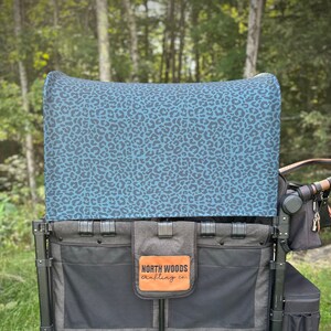 May include: A black wagon with a teal leopard print canopy. The wagon has two large storage compartments and a smaller compartment on the side. The wagon has a black leather patch with the text "NORTH WOODS crafting co."