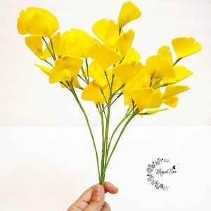 May include: A bouquet of artificial yellow ginkgo biloba leaves attached to thin green stems. The fan-shaped leaves are vibrant yellow with a textured appearance. A small logo with the text Magical Flora is visible in the lower right corner.