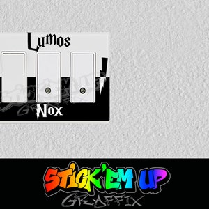 May include: A white light switch cover with black accents. The top half of the cover is white with the word "Lumos" in black lettering. The bottom half of the cover is black with the word "Nox" in white lettering. The cover has three light switch toggles.