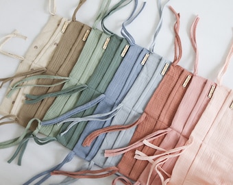 May include: A set of seven fabric crib bumpers in various colors, including beige, green, blue, and pink. Each bumper has a simple design and is tied with long fabric ties.