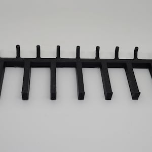 May include: Black metal rack with 12 hooks for hanging items. The rack is about 12 inches long.