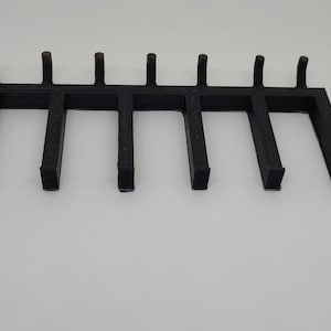 Pode incluir: Grelha de lareira de metal preto com nove barras verticais e uma barra horizontal que as conecta. A grelha é projetada para manter as toras no lugar.