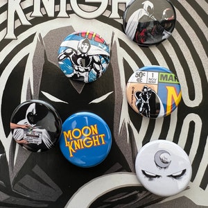 May include: Six round buttons featuring the Marvel Comics character Moon Knight. The buttons feature different images of Moon Knight, including a close-up of his face, a full-body shot, and a scene from the comics. The buttons are all white with black accents and have a glossy finish.