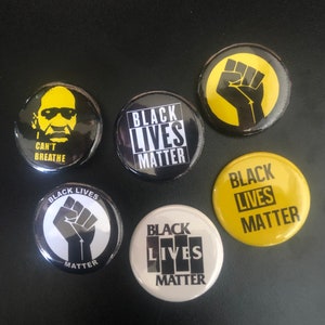 May include: Six round black and yellow buttons with the phrase "Black Lives Matter" in different styles. One button features a black fist, another features a black and white image of a man with the text "I Can't Breathe", and another features a black and white image of a man with the text "I Can't Breathe".