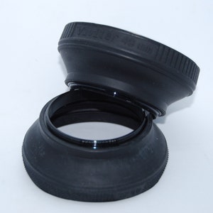 May include: Two black lens hoods, one stacked on top of the other. The top hood has the text "Vivitar 49 mm" printed on it.