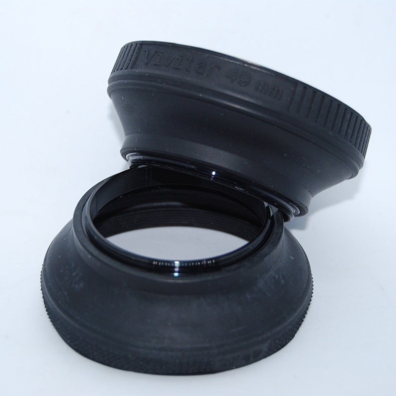 May include: Two black lens hoods, one stacked on top of the other. The top hood has the text "Vivitar 49 mm" printed on it.