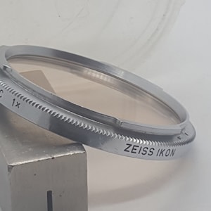 May include: A silver metal filter ring with the text "Color C 1x" and "ZEISS IKON" engraved on it.