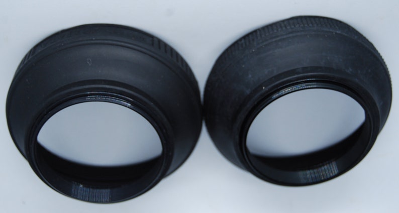 May include: Two black rubber lens hoods for a camera lens. The hoods are designed to block out stray light and glare.