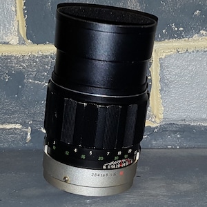 May include: A black camera lens with a silver ring and markings. The lens has a depth of field scale and aperture markings. The lens is 28mm, 4, 5.6, 8, 11, 16.
