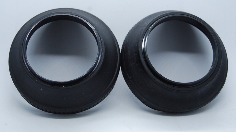 May include: Two black lens hoods for camera lenses. The hoods are made of a rubber-like material and have a smooth, black finish.