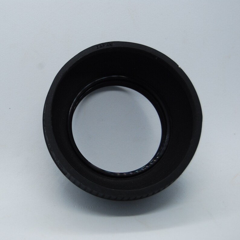 May include: Black rubber lens hood with the word "JAPAN" printed on the top.
