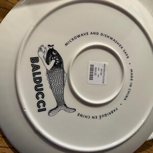 Puede incluir: Plato de cer&aacute;mica blanco con una ilustraci&oacute;n de pez en blanco y negro y la palabra "BADUCCI". El plato est&aacute; etiquetado como "MICROONDAS Y LAVAVAJILLAS" y "MADE IN CHINA".