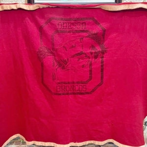 May include: A red blanket with a white border. The blanket features a black and white logo that reads "Odessa Broncos" with a horse's head inside the "O".