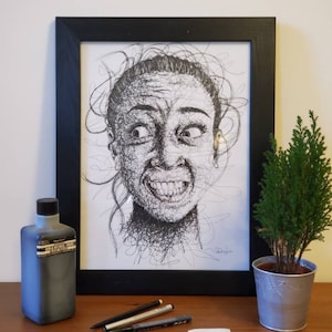 May include: A framed black and white line drawing of a person's face with a surprised expression. The drawing is made up of many small, intricate lines. The frame is black and the mount is white. There is a bottle of drawing ink, a few pens, and a white eraser on a wooden table.