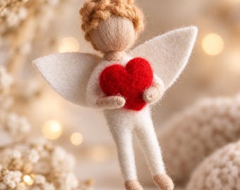 May include: A felted wool angel ornament featuring a beige head with curly hair, white wings, and a white body. The angel holds a bright red felt heart in its hands and is suspended by a thin white string for hanging purposes.