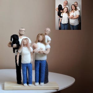 Könnte beinhalten: Ein gefilztes Familienfiguren-Set, einschließlich eines Hundes, in einer Familienporträtpose. Die Figuren tragen weiße Hemden und blaue Jeans. Der Hund ist schwarz. Die Familie steht auf einer Holzbasis. Ein gerahmtes Foto der Familie befindet sich im Hintergrund.