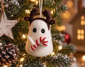 May include: A white felted ornament shaped like a ghost wearing brown reindeer antlers. The ghost has two small black eyes and is holding a red and white striped candy cane. A thin white string is attached to the top for hanging on a tree.