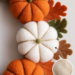 May include: A decorative wreath featuring felted wool pumpkins in shades of orange, white, and yellow, accented with green and brown felt leaves. The text reads HANDMADE FROM NATURAL WOOL, with a circular inset showing a close-up of the wool texture.