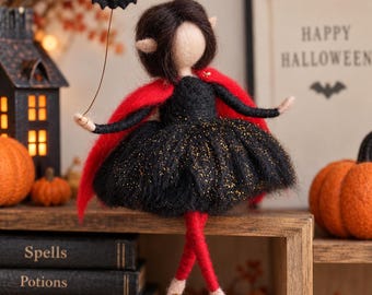 May include: A needle-felted doll with dark brown hair and pointed ears, wearing a black dress with gold glitter accents and a red cape. The doll holds a thin wire topped with a small black bat and has red legs with light-colored feet.