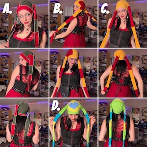 May include: A collection of jester-style hats featuring long, dangling ear flaps in various color combinations including olive green, red, yellow, and bright green, with one hat displaying a light blue heart patch on the crown.