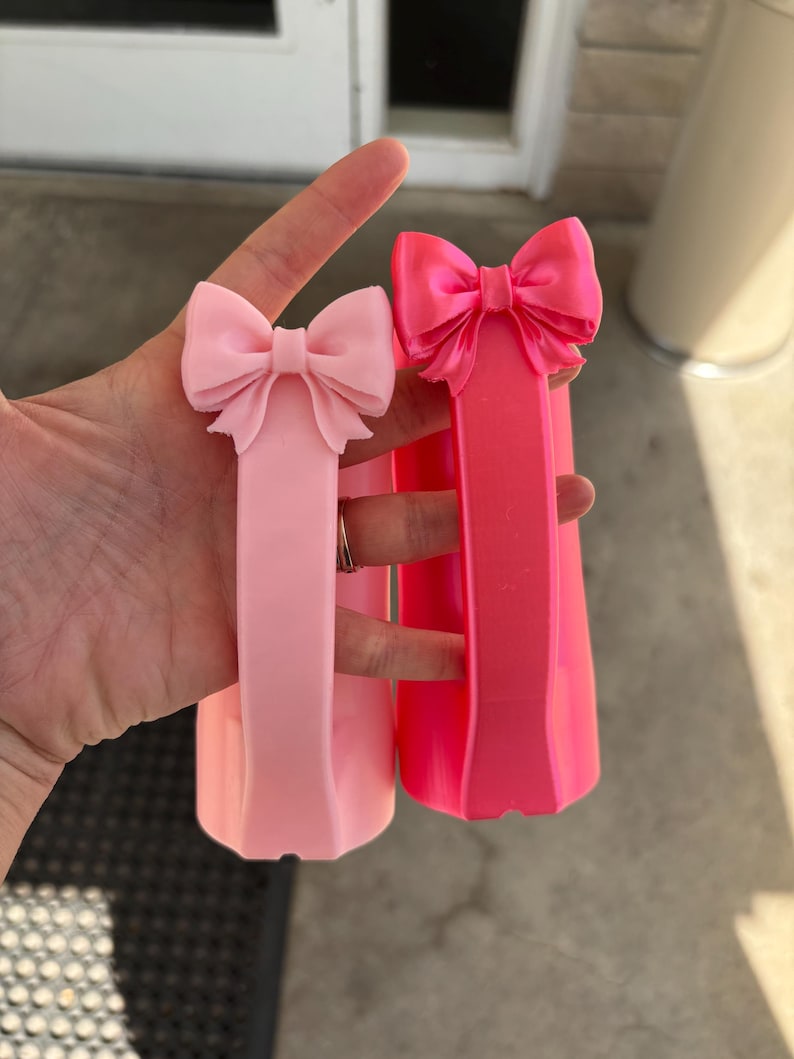 May include: Two pink bow-shaped hair accessories. One is a lighter shade of pink, and the other is a vibrant, hot pink. Both have a rectangular base. The bows are at the top of the rectangular base.