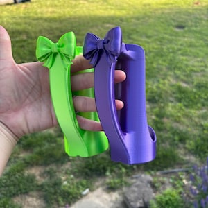 May include: Two decorative, 3D-printed handles in bright colors. One is lime green, the other is purple. Each handle features a bow at the top. The handles are designed with a curved shape and a grip.