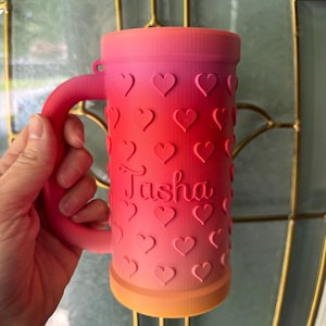 K&ouml;nnte beinhalten: Ombre-farbener Becher mit Henkel, von Rosa nach Orange verlaufend. Der Becher ist mit herzf&ouml;rmigen Aussparungen und dem Namen "Tasha" verziert. Personalisierte Trinkbecher.