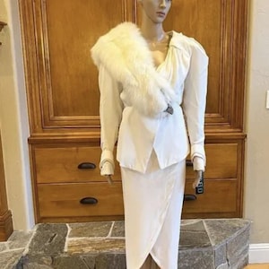 May include: A white dress with a white fur stole. The dress has a wrap-style skirt and a fitted bodice. The dress is on a mannequin.