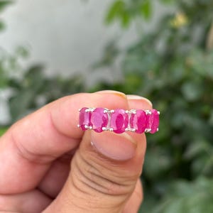 May include: A silver ring with a row of oval-shaped pink gemstones.