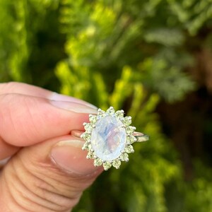 May include: A silver ring with a large oval moonstone surrounded by a halo of smaller green peridot stones.