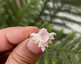May include: A silver ring with a pear-shaped pink gemstone surrounded by smaller clear gemstones.