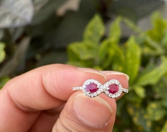 Op de afbeelding: Een zilveren oneindigheidsring met twee rode robijnen die zijn gezet in een halo van kleinere diamanten.