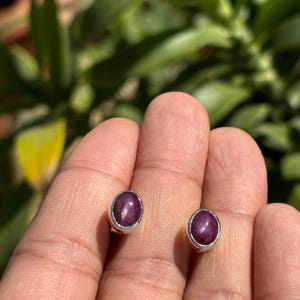 May include: A pair of silver stud earrings with a round, dark red star ruby gemstone in each.