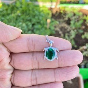 May include: A silver turtle pendant necklace with a large green oval gemstone surrounded by smaller clear gemstones.