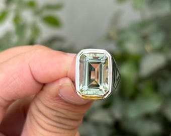 May include: A silver ring with a large, light green emerald-cut gemstone.