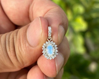 May include: A silver pendant with a moonstone oval gemstone surrounded by a halo of smaller clear gemstones.