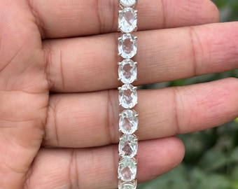 May include: A silver bracelet with a row of clear oval-shaped gemstones. The bracelet is on a person's hand.