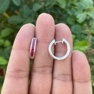 Op de afbeelding: Een paar zilveren creolen, waarvan er één een rij rode vierkante edelstenen heeft.