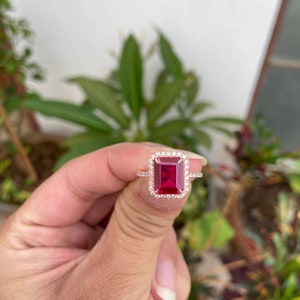 May include: A rose gold ring with a large, emerald-cut ruby surrounded by a halo of smaller diamonds.