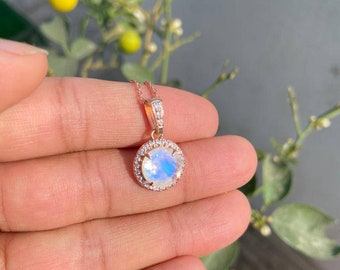 May include: A rose gold pendant necklace with a round moonstone surrounded by a halo of smaller clear stones.