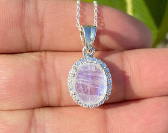 Può includere: Una collana d'argento con un ciondolo ovale in pietra di luna bianca circondato da un'aureola di piccole pietre di zircone cubico trasparenti.
