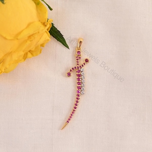 May include: A gold pendant shaped like a curved sword or dagger, featuring a central row of round pink rubies and a parallel row of round white diamonds. The piece includes a small gold bail at the top for attachment to a necklace chain.