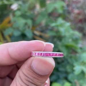 Pode incluir: Uma fina banda de prata com uma fileira de pedras preciosas quadradas cor-de-rosa.