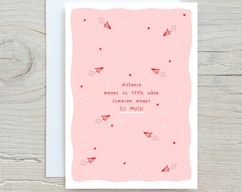 May include: Pink card with a white border and a wavy edge. The card has a red heart pattern and red paper airplanes. The text on the card reads "distance means so little when someone means SO MUCH".