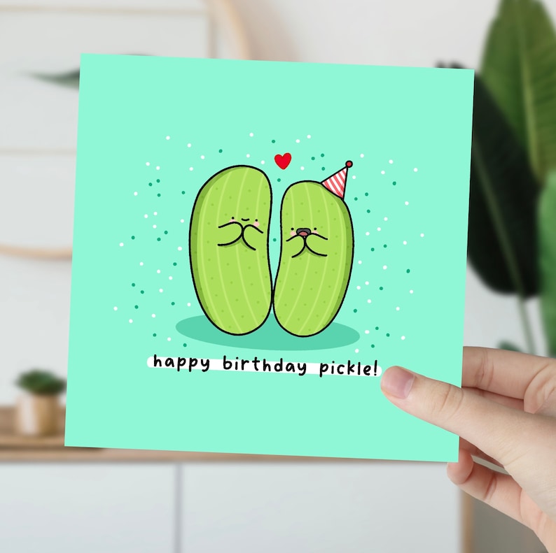 May include: A light green birthday card with two cartoon pickles wearing party hats. The card has a light blue background with white polka dots and the text "happy birthday pickle!"