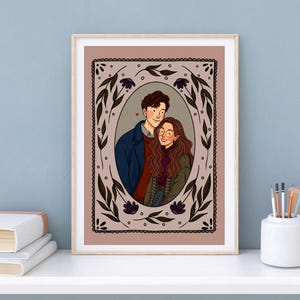 May include: A framed digital illustration featuring a couple in an oval portrait. The person on the left wears a dark blue coat over a red sweater, while the person on the right has long brown hair, glasses, and a green jacket. The border is floral.